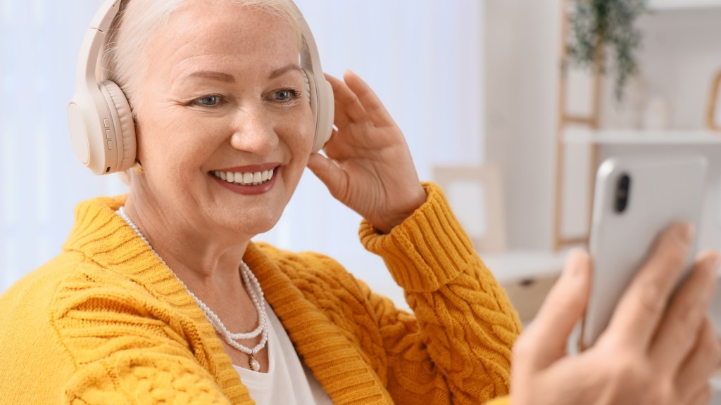 Woman wearing yellow cardican wearing headphones and holding her phone up